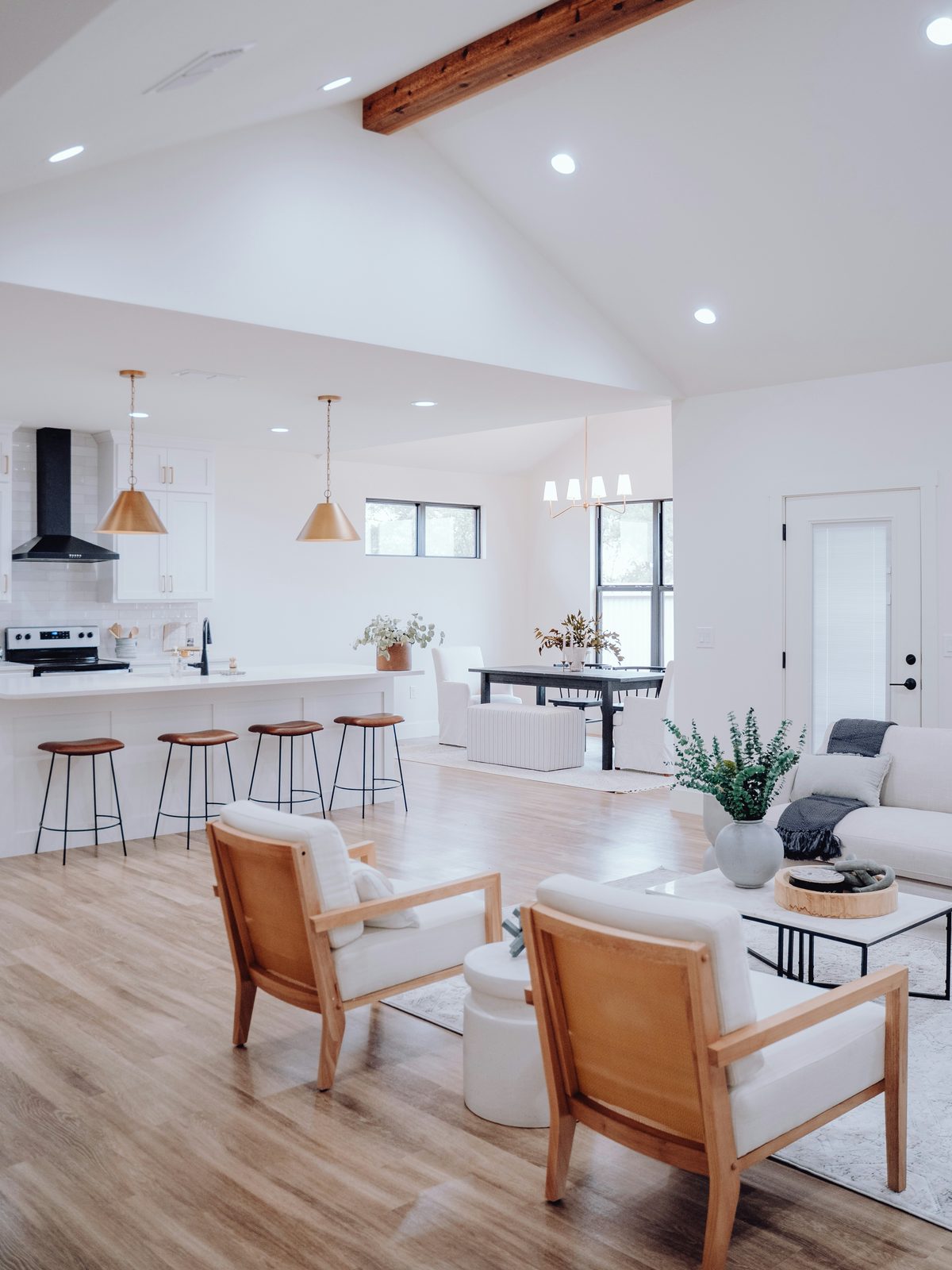 Open-plan living room, kitchen, and dining area with a vaulted ceiling and light wood-look plank flooring