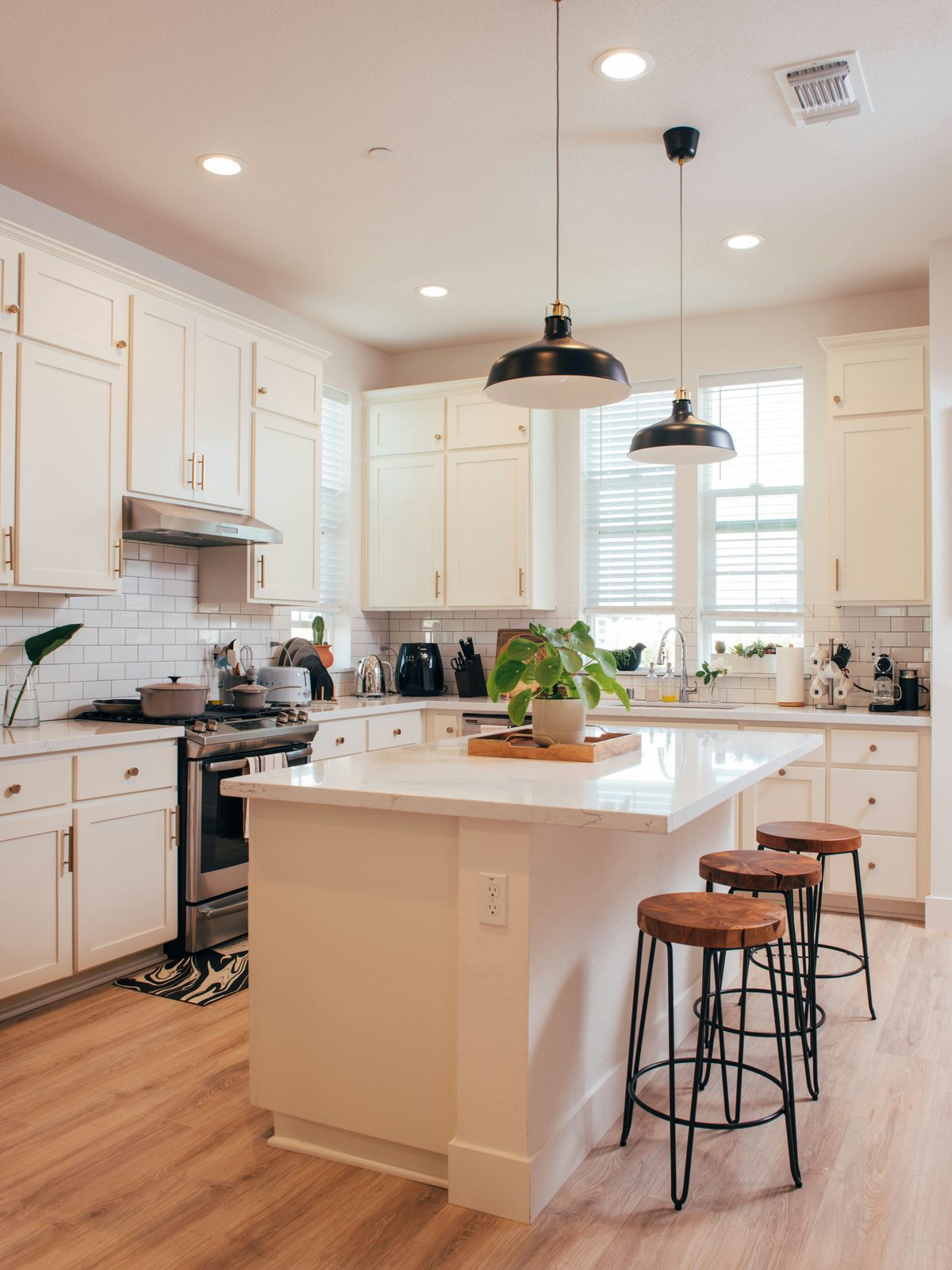 White kitchen with an island, wood-top stools, black pendant lights, and light wood-look plank flooring