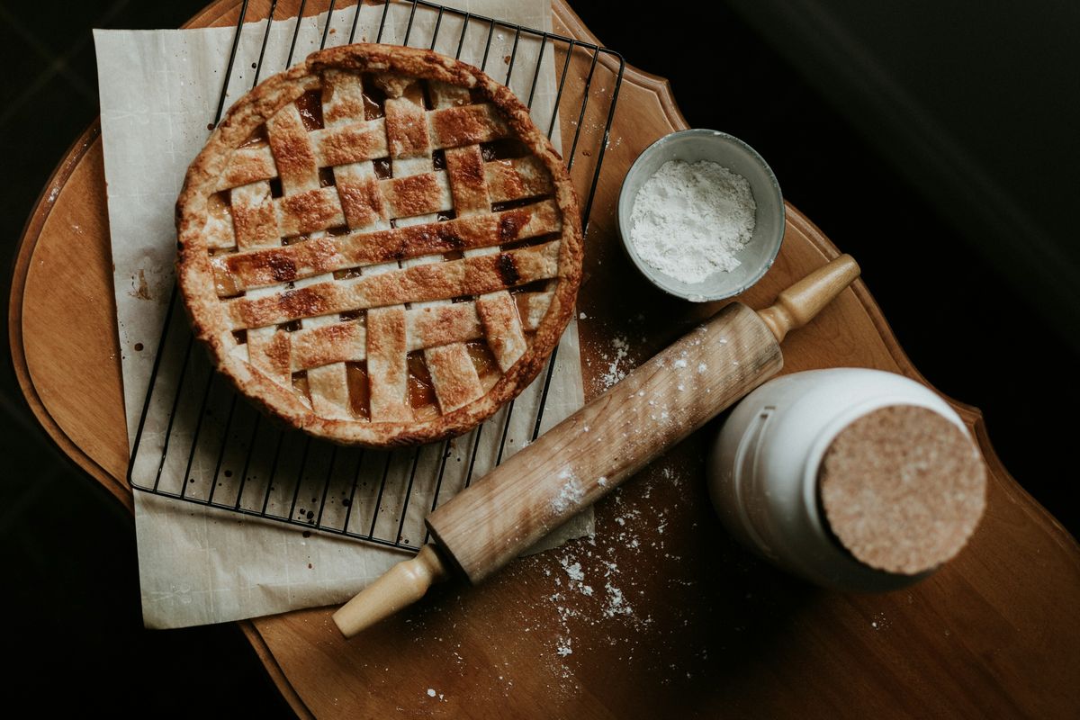 A lattice-top fruit pie on a wire rack next to a rolling pin and a bowl of flour