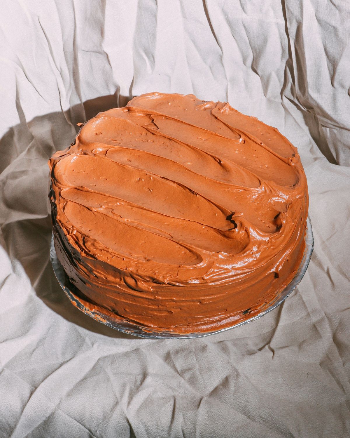 A two-layer cake with swooped caramel-colored frosting on a glass plate