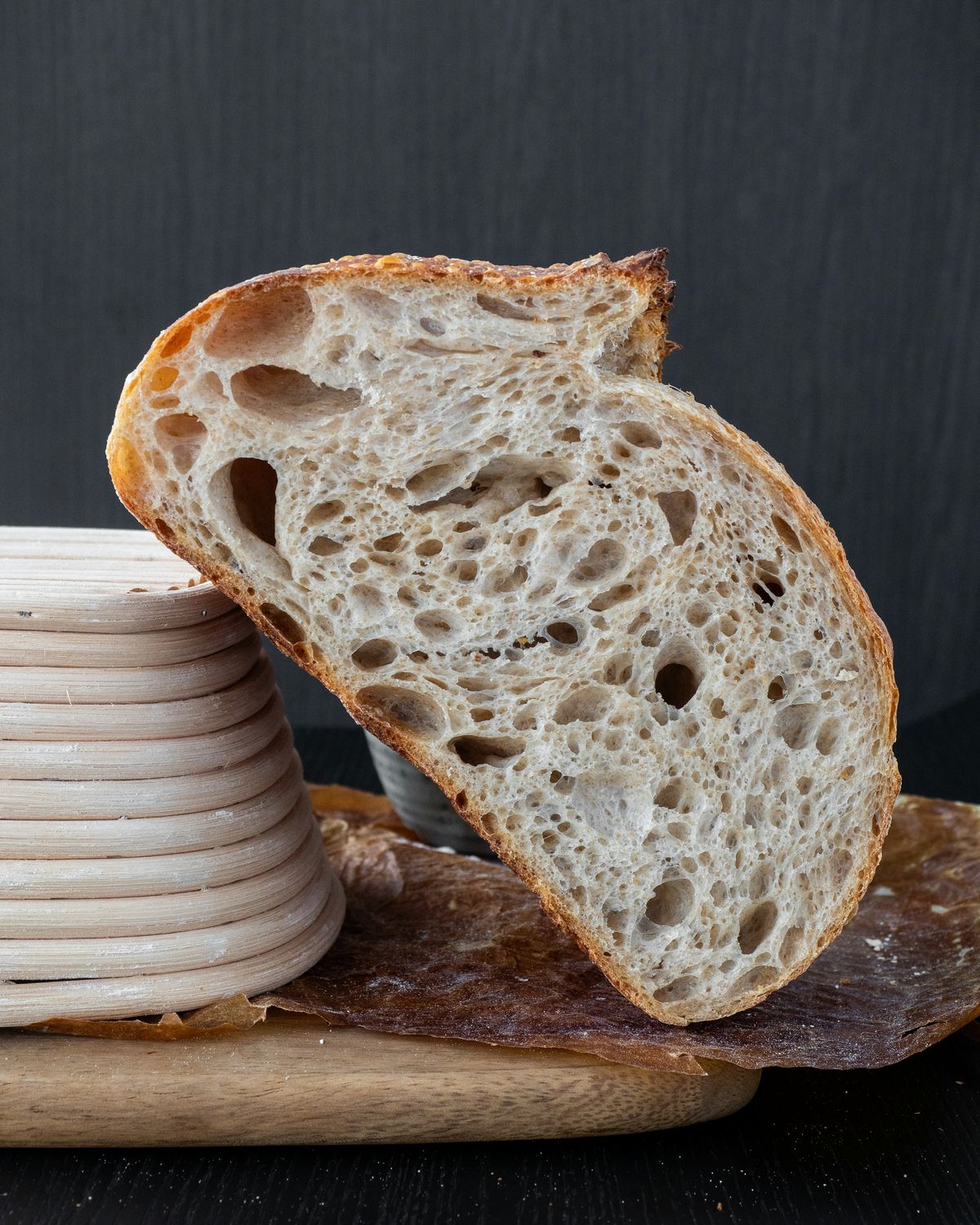 Half a sourdough loaf with an open crumb, standing against a stack of cane proofing baskets