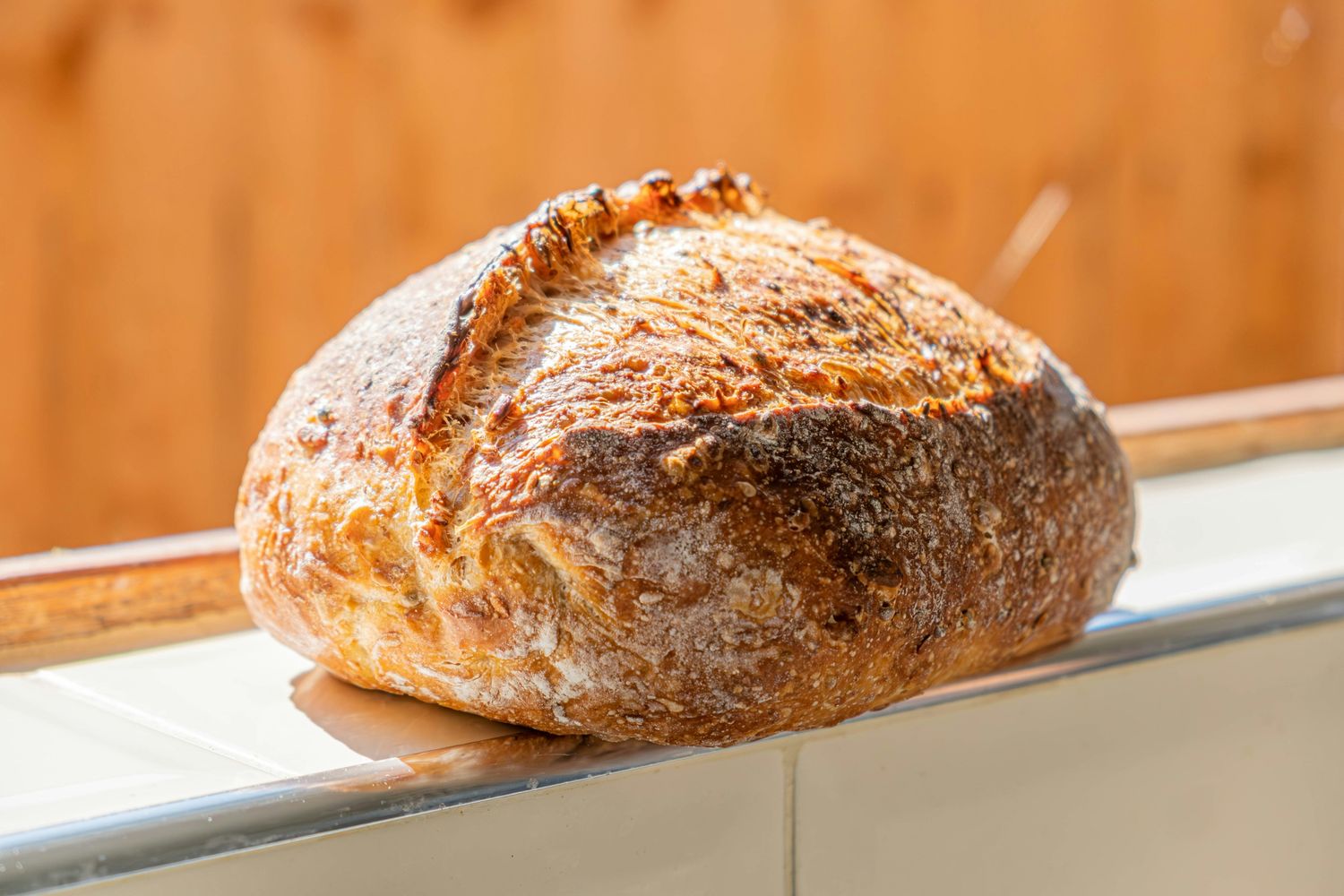 A seeded sourdough boule on a tiled ledge in warm light